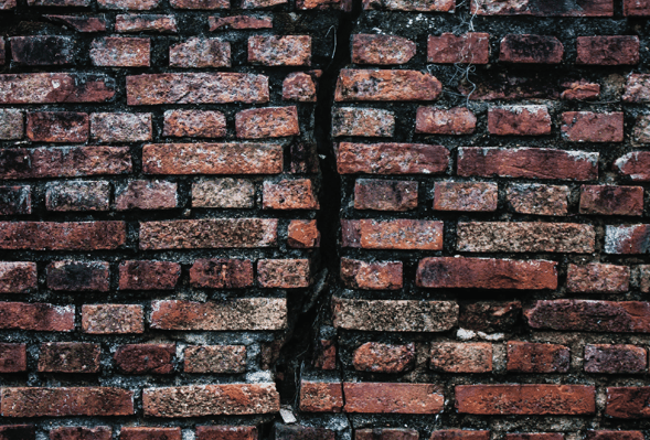 A brick wall with a large crack down the middle of the wall